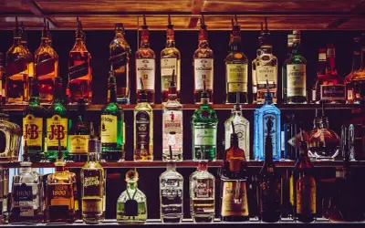 Rzędy butelek alkoholi, w tym whisky, ginu i likierów, na półkach baru.