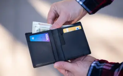 Dłonie wkładają pieniądze i kartę Visa do czarnego portfela.
