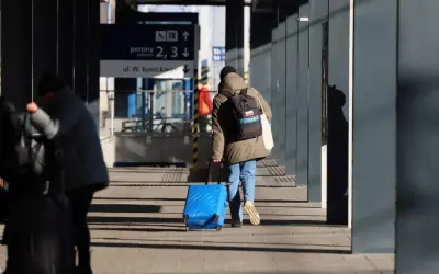 Osoba z niebieską walizką na kółkach i plecakiem idzie po peronie.