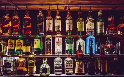 Rzędy butelek alkoholi, w tym whisky, ginu i likierów, na półkach baru.