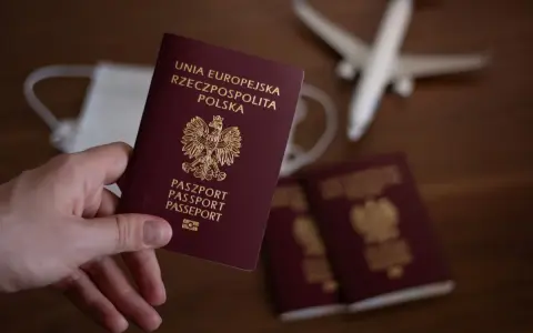 Dłoń trzyma polski paszport. W tle maseczka, samolot i inne paszporty.