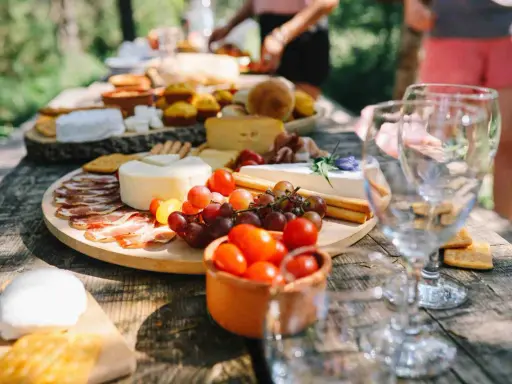 Stół piknikowy z serami, wędlinami, winogronami, pomidorkami i pieczywem.