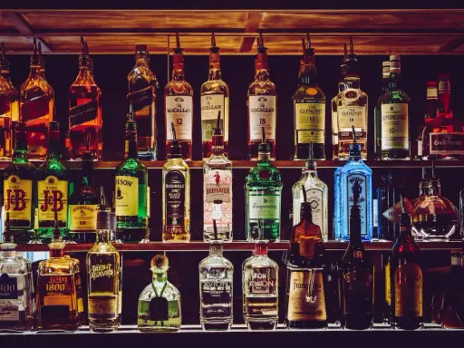 Rzędy butelek alkoholi, w tym whisky, ginu i likierów, na półkach baru.
