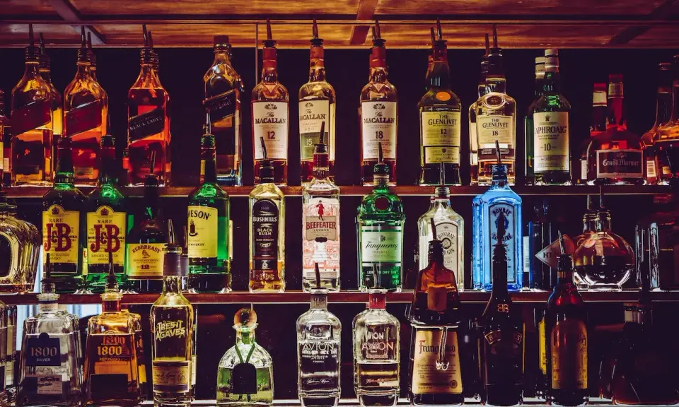 Rzędy butelek alkoholi, w tym whisky, ginu i likierów, na półkach baru.