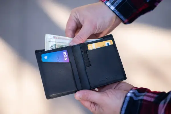 Dłonie wkładają pieniądze i kartę Visa do czarnego portfela.