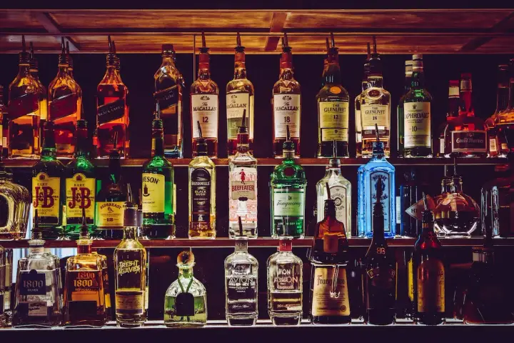 Rzędy butelek alkoholi, w tym whisky, ginu i likierów, na półkach baru.